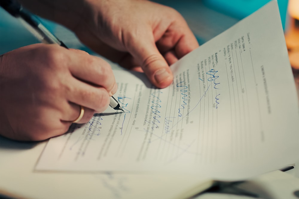 Mãos assinando um documento com caneta sobre uma mesa