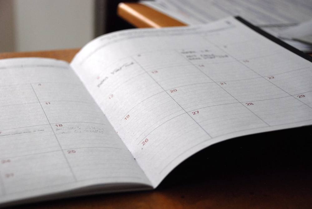 Agenda de planejamento aberta sobre uma mesa de madeira, com um calendário mensal visível
