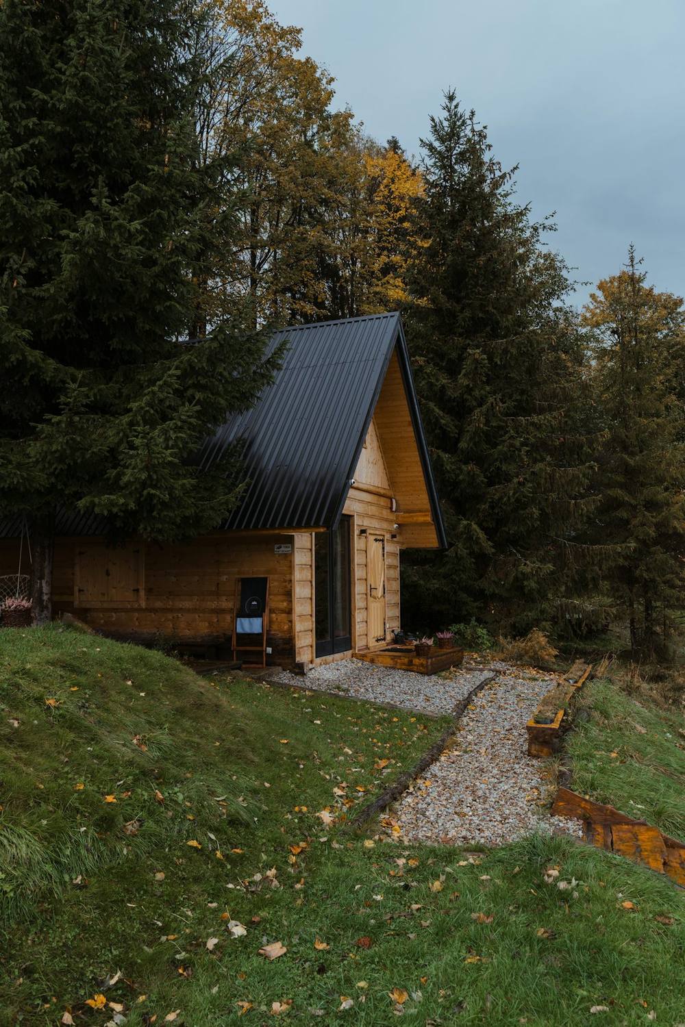 Cabana de madeira isolada em meio a uma floresta densa, com caminho de pedras até a porta